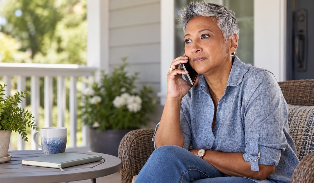A mature Black woman with short silver hair has a private supportive phone conversation on a plain covered porch.